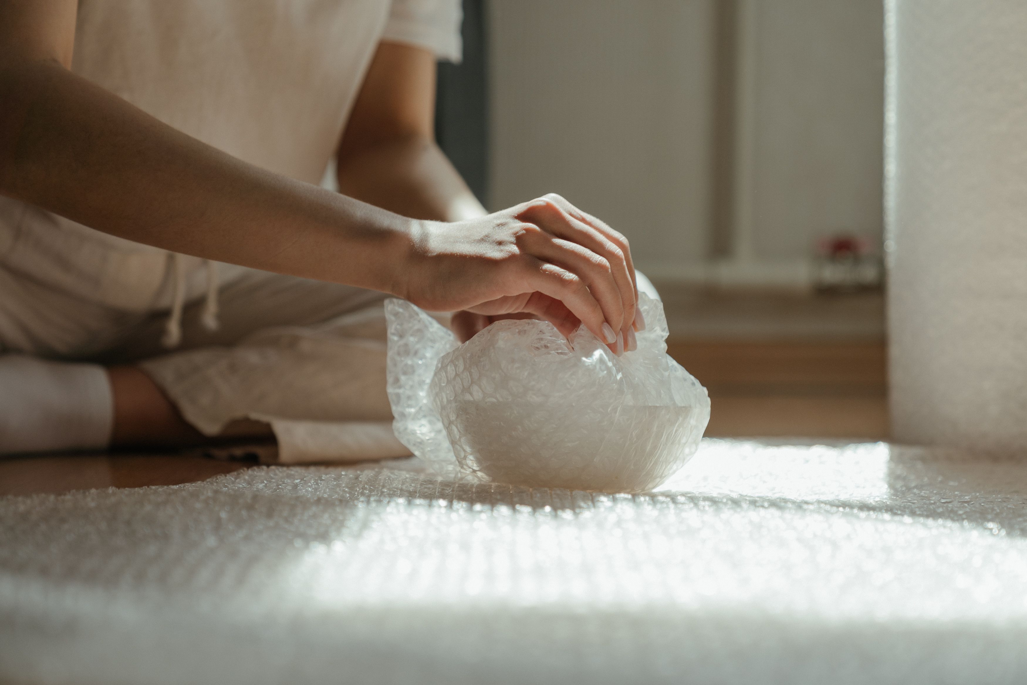 Hands wrapping an object in bubble wrap as protective cushioning before packing