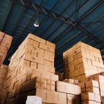 High stacks of cardboard boxes organized and stored in a warehouse with a metal ceiling