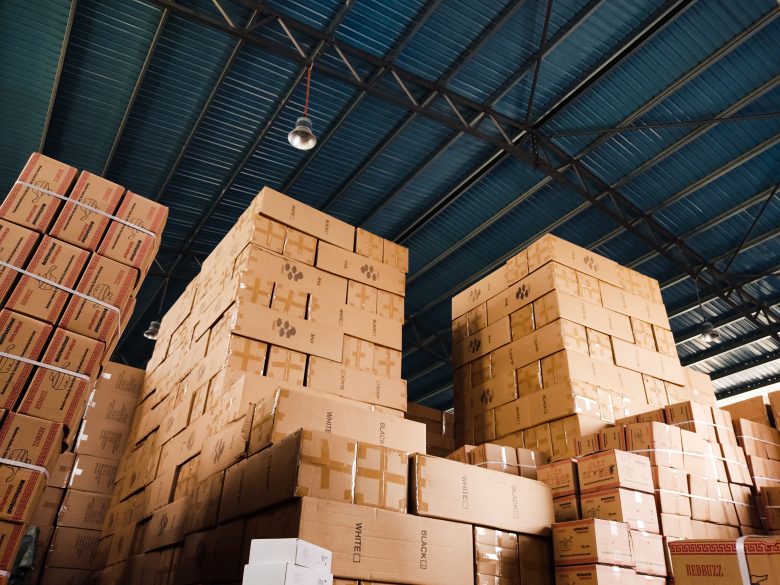 High stacks of cardboard boxes organized and stored in a warehouse with a metal ceiling