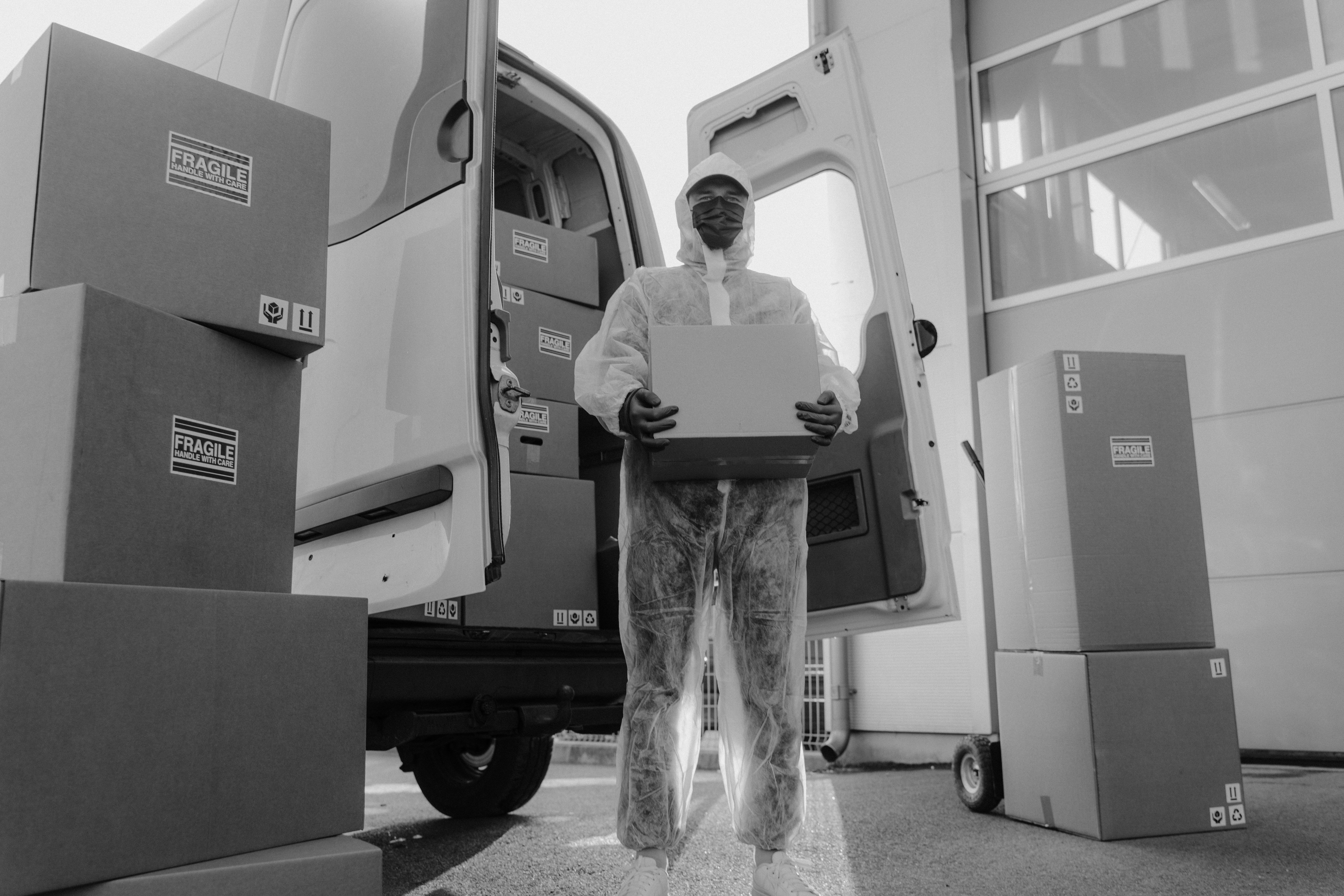 Delivery worker in protective gear carrying packages from a delivery van for safe transport
