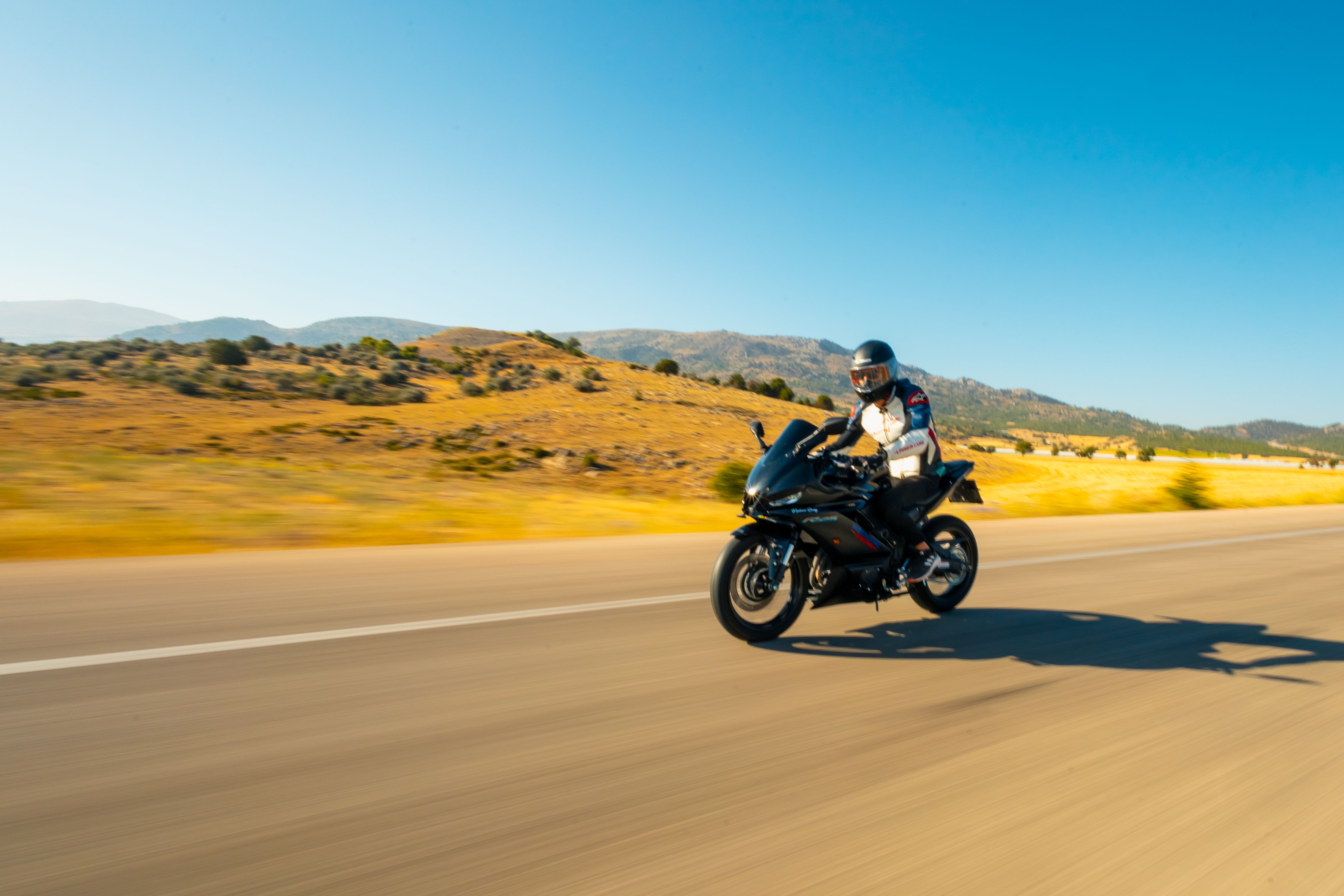 Motorcyclist riding fast on a wide open desert road with strong crosswinds