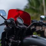 Close-up of motorcycle handlebars with a red windshield providing wind protection