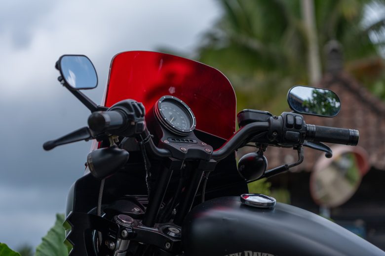 Close-up of motorcycle handlebars with a red windshield providing wind protection