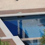 Modern swimming pool bordered by durable-looking wood decking on a sunny day.