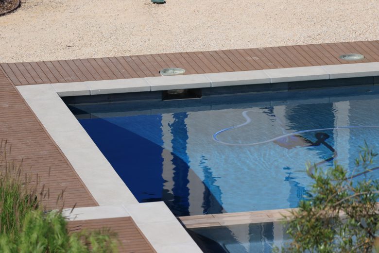 Modern swimming pool bordered by durable-looking wood decking on a sunny day.