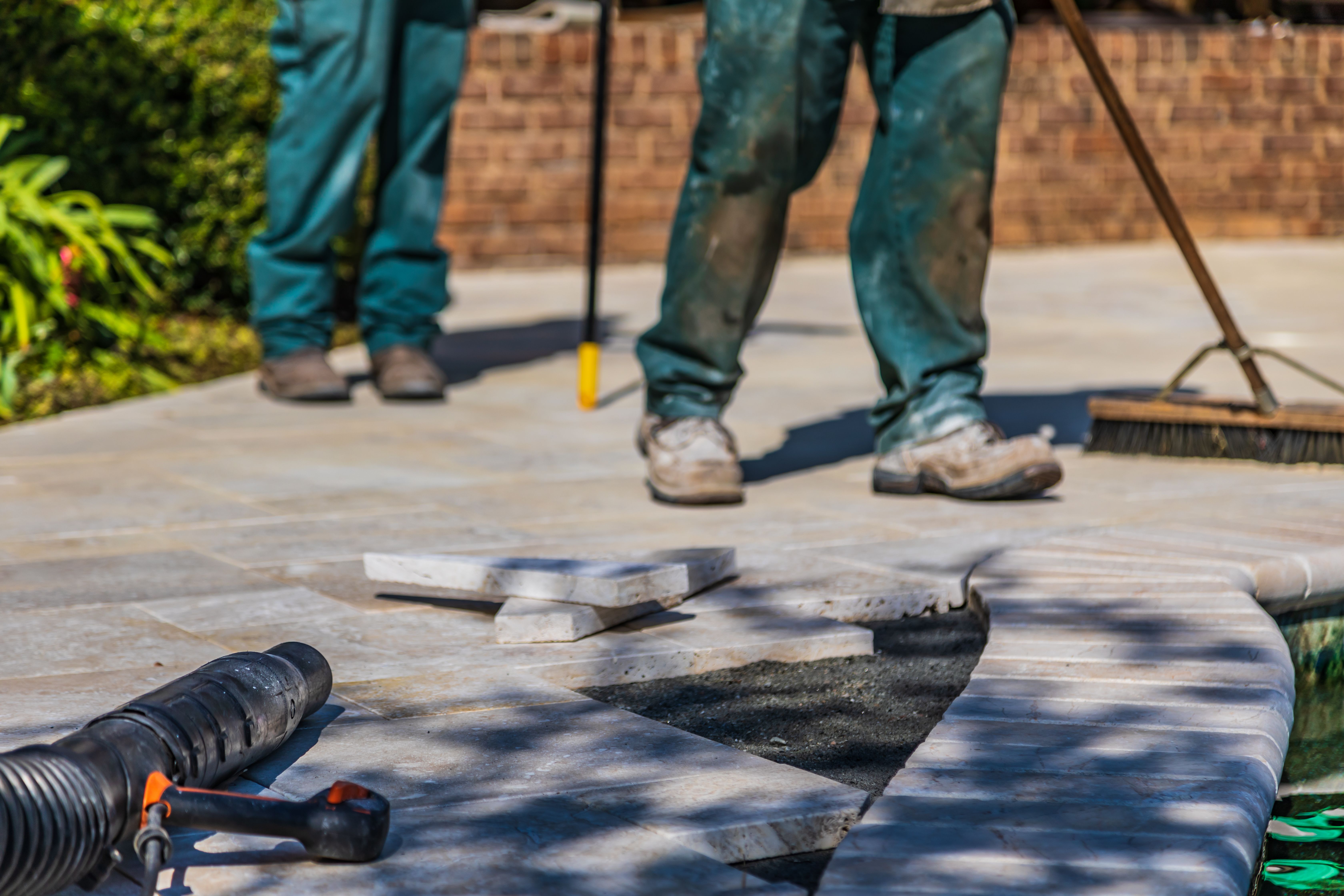 Workers installing outdoor patio tiles in bright sunlight, illustrating durable hardscaping materials.